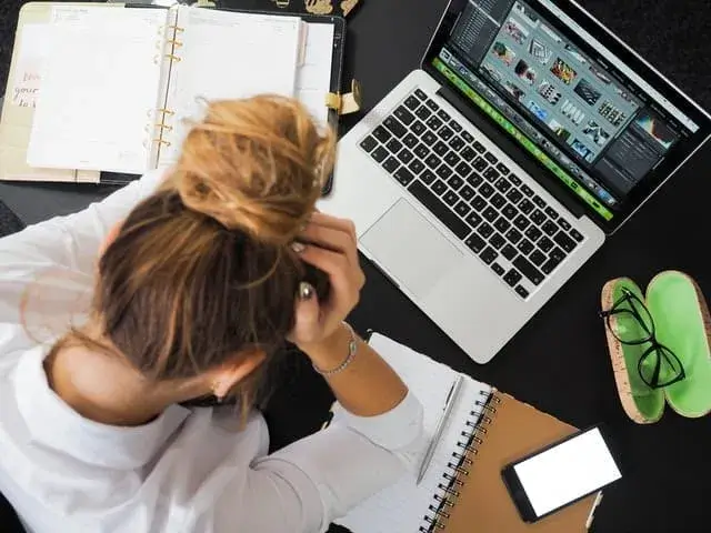 Stressed woman at desk with laptop and smartphone, highlighting modern multitasking challenges.