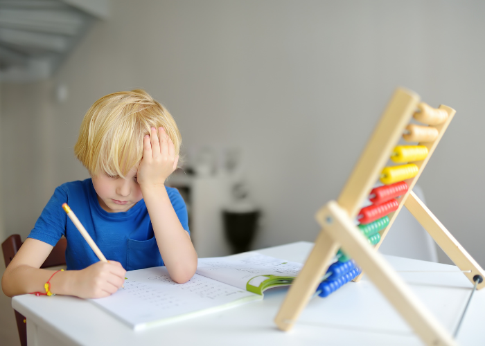 A young boy sits at a desk, focused on a paper with a pencil, reflecting signs of anxiety and ADHD symptoms.