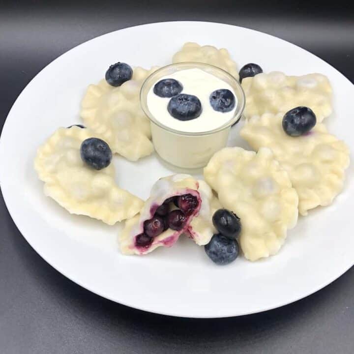 A plate with blueberry dumplings, also known as pierogi, and a bowl of yogurt.