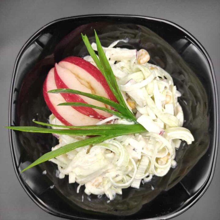 Polish leek salad garnished with apple slices in a black bowl.