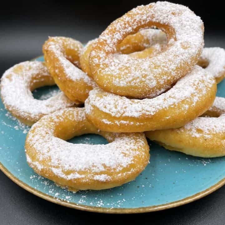Polish cheese donuts on a blue plate with powdered sugar on top.