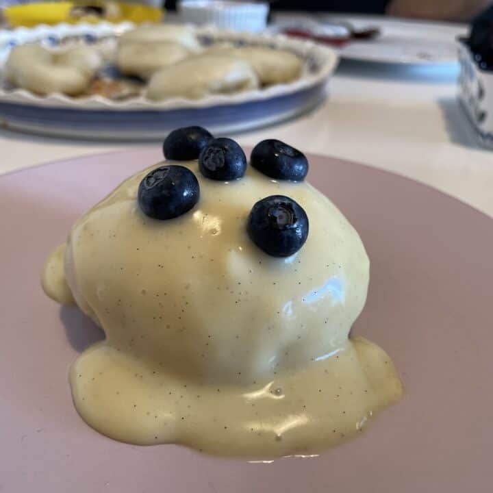A dessert with vanilla sauce and blueberries on a plate of Polish Steamed Buns.