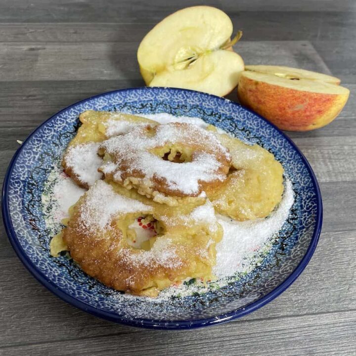 Dusted Polish apple pancakes without yeast on a decorative blue plate with sliced apples to the side.
