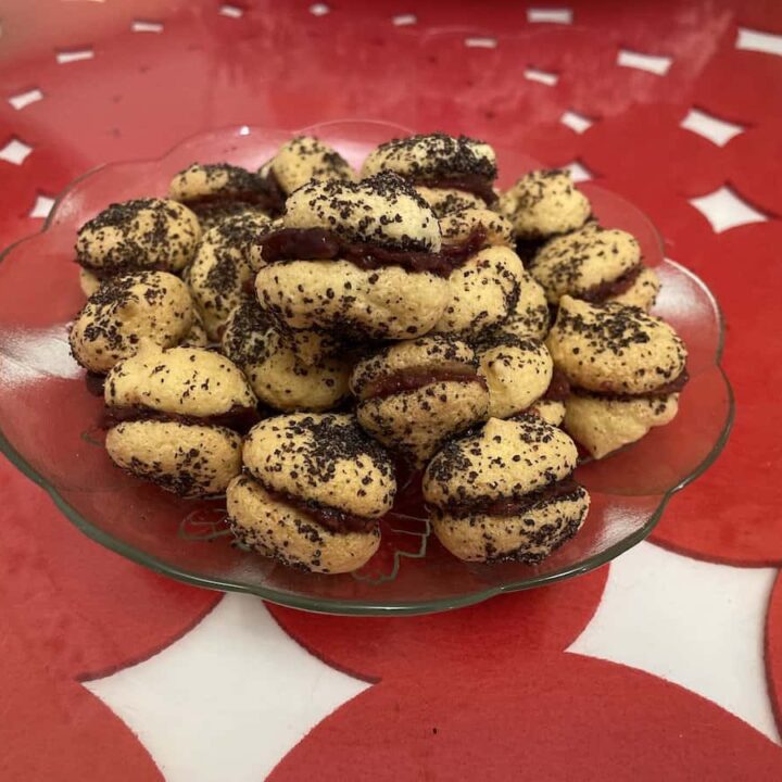 A plate of round Polish poppy seed cookies sprinkled with poppy seeds, displayed on a table with a red and white patterned tablecloth.