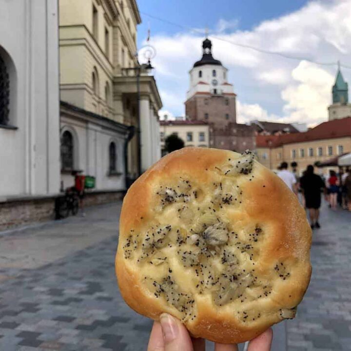 A hand holding Polish Onion Rolls with a European town square in the background.