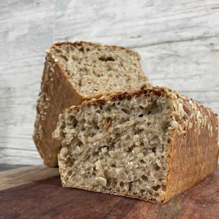 A loaf of Polish sunflower seed bread sliced in half on a wooden board with a rustic background.