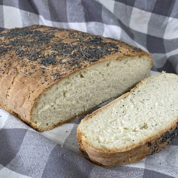 A loaf of poppy seed chleb pszenny partially sliced, resting on a checkered cloth.