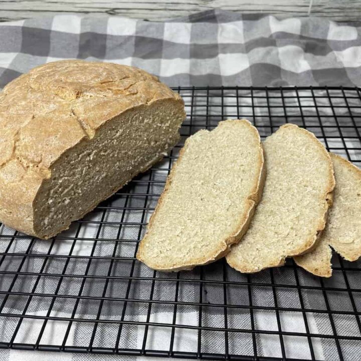 A loaf of freshly baked Polish buttermilk rye bread, partially sliced, on a wire cooling rack.