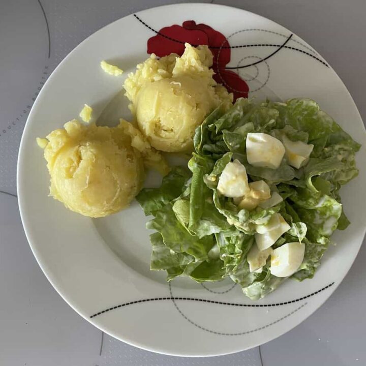 A plate with two scoops of yellow mashed potatoes and a Polish egg and lettuce salad with chopped hard-boiled eggs.