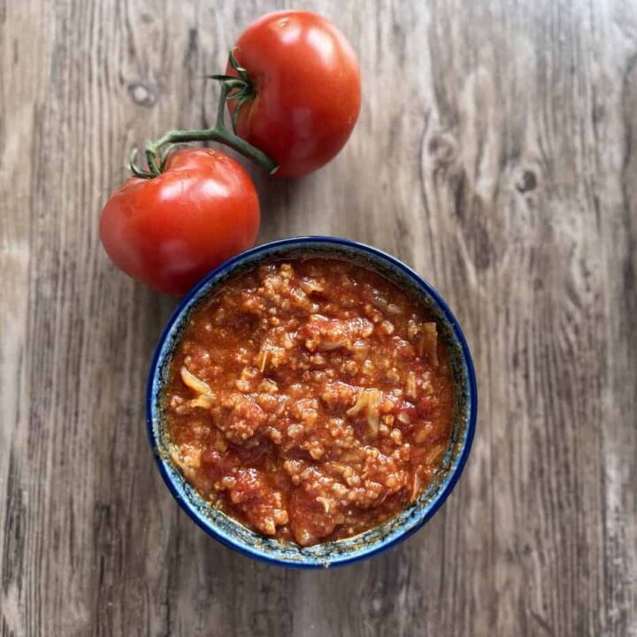 A bowl of tomato-based Polish stuffed cabbage soup sits on a wooden surface next to two fresh tomatoes still attached to the stem.