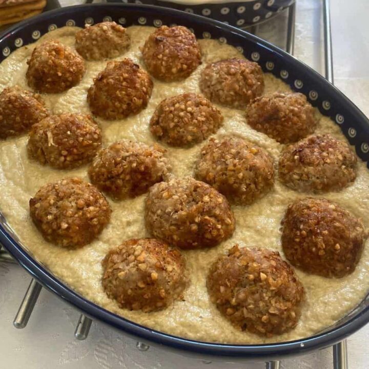 A baking dish filled with hreczanyki, resembling Polish patties, arranged in rows and nestled in a creamy white sauce.