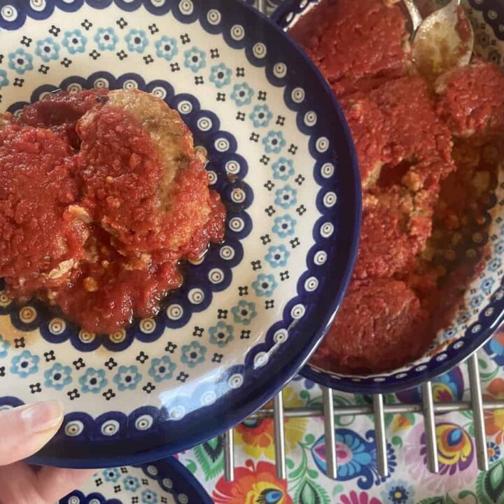 A hand holds a plate with stuffed artichokes topped with tomato sauce, reminiscent of a Gołąbki Casserole, above a larger dish containing more servings on a colorful tablecloth. Perfect for those seeking an unstuffed cabbage rolls vibe in a quick recipe format.