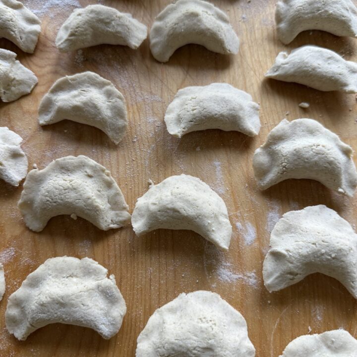 Authentic pierogi are arranged in neat rows on a wooden surface, each uncooked dumpling lightly dusted with flour.