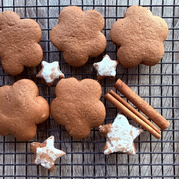 Flower-shaped and star-shaped Polish gingerbread cookies with white icing rest on a cooling rack next to three sticks of cinnamon, all set atop a wooden surface.