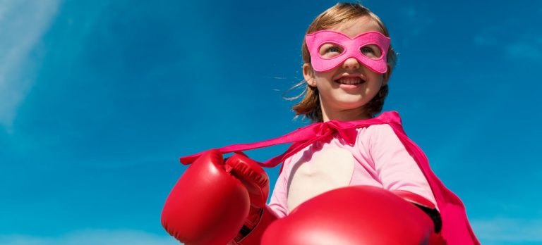Mädchen in Superheldenkostüm mit Boxhandschuhen zeigt eine Power-Pose zur Stärkung des Selbstbewusstseins.