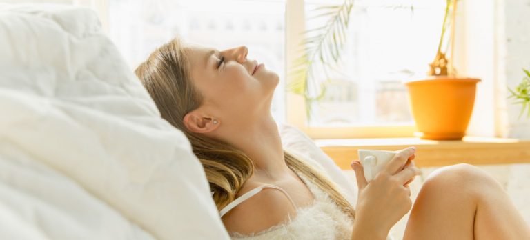 Frau genießt Sonnenlicht durch ein Fenster, als Symbol für die positive Wirkung der Lichttherapie.