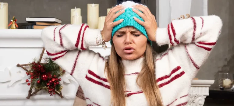 Frau in Weihnachtsstrickpulli und Mütze hält sich gestresst den Kopf – ein Sinnbild für Weihnachtsstress und Perfektionismus.