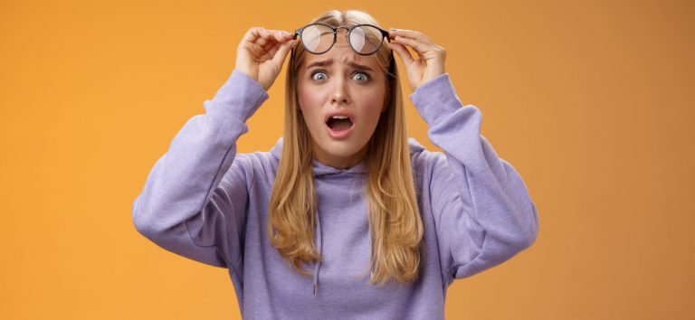 Eine junge Frau hebt überrascht ihre Brille an. Dies symbolisiert, wie wir durch kognitive Verzerrungen die Realität verzerrt wahrnehmen.