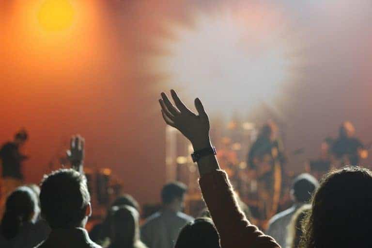 A crowd with raised hands faces a brightly lit stage where a band is performing; the background glows warmly&mdash;an energy that matches any festival in Poland, known for jaw dropping facts and vibrant music scenes.