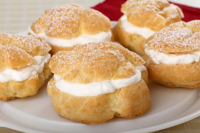 A plate with a group of Polish pastries, known as cream puffs or ptysie, topped with whipped cream and powdered sugar.