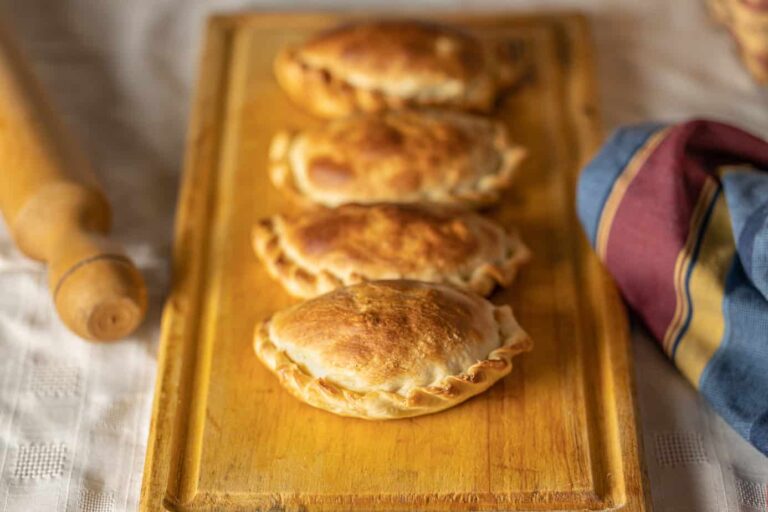 Freshly baked pierogi on a wooden board with a rolling pin and cloth napkin nearby.