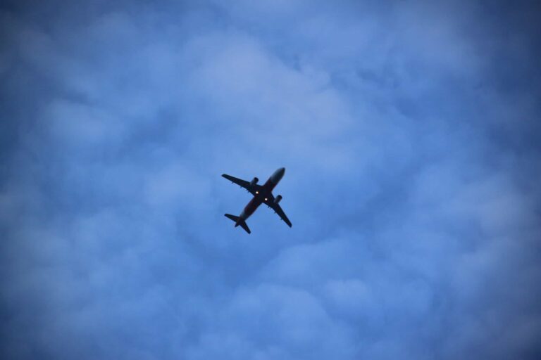 A commercial airplane is flying overhead against a blue sky with scattered clouds.