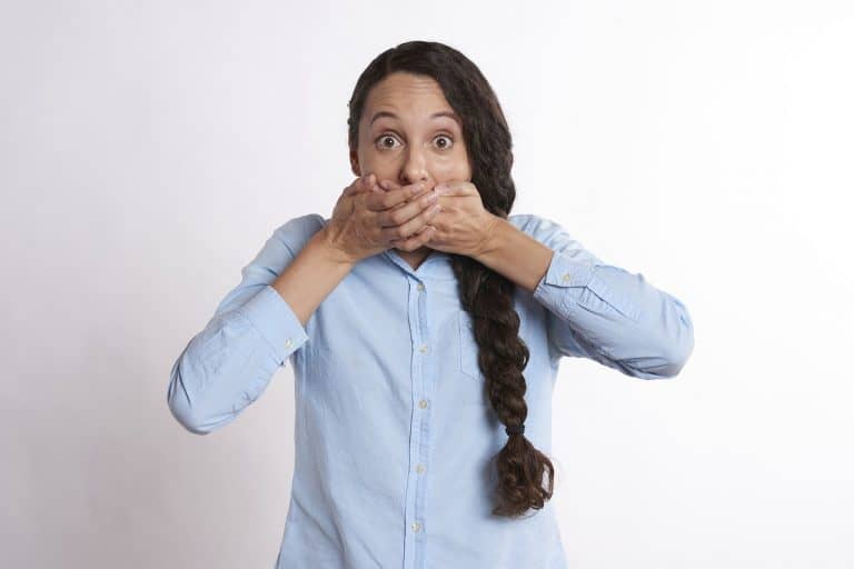 A woman with long dark hair in a braid covers her mouth with both hands, looking surprised, as if she just heard some jaw-dropping facts about Poland, against a plain white background.