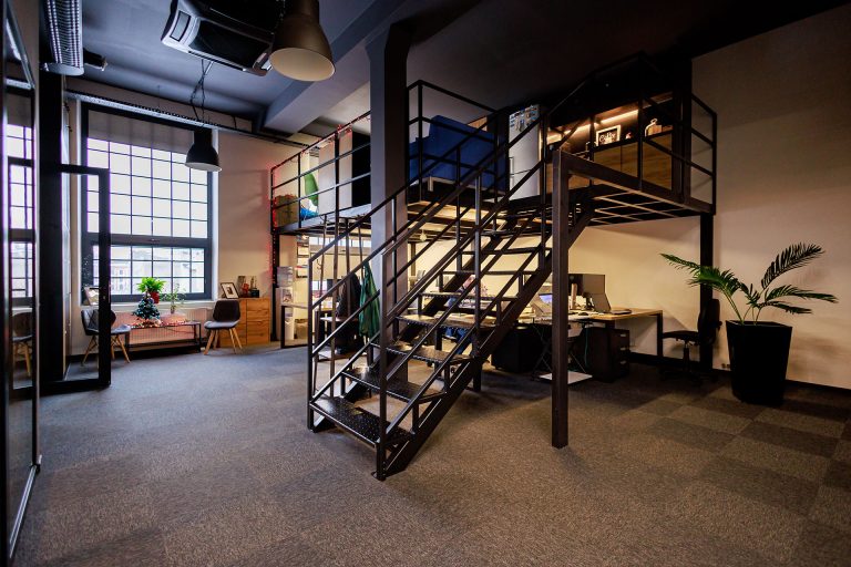 Industrialne wnętrze Centrum Szkoleniowego NT Group z antresolą i schodami.