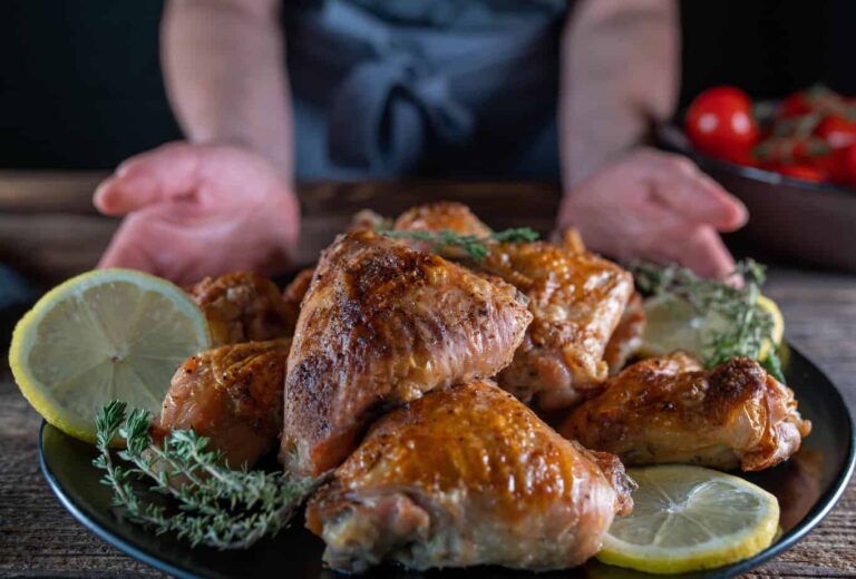 A person presenting a plate of top Polish roasted chicken garnished with lemon slices and herbs, with fresh tomatoes in the background.