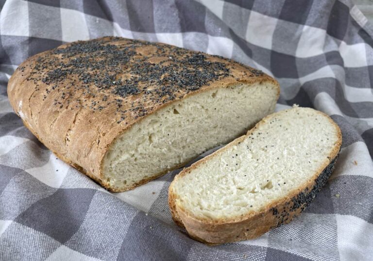 A loaf of poppy seed chleb pszenny partially sliced, resting on a checkered cloth.