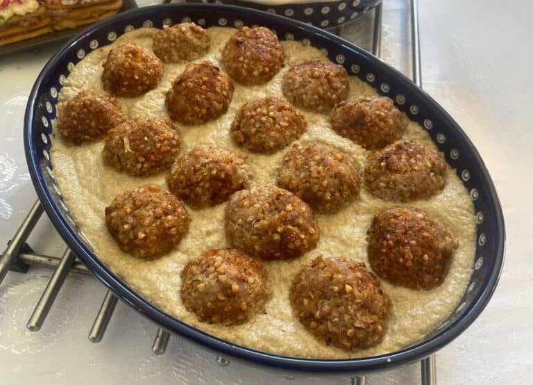 A baking dish filled with hreczanyki, resembling Polish patties, arranged in rows and nestled in a creamy white sauce.