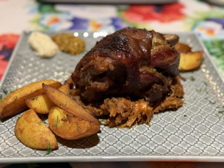 A plate featuring golonka w piwie, roasted to perfection on a bed of sauerkraut, served alongside crispy potato wedges, tangy mustard, and sharp horseradish.