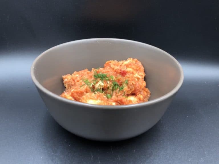 A bowl of Kurczak W Sosie Pomidorowym in a gray bowl on a black surface.