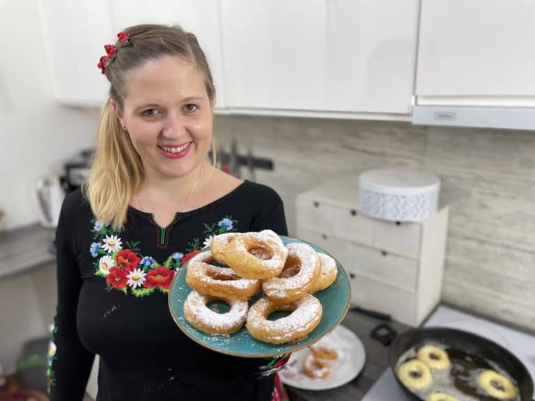 A woman holding a plate of Polish cheese donuts in her kitchen.