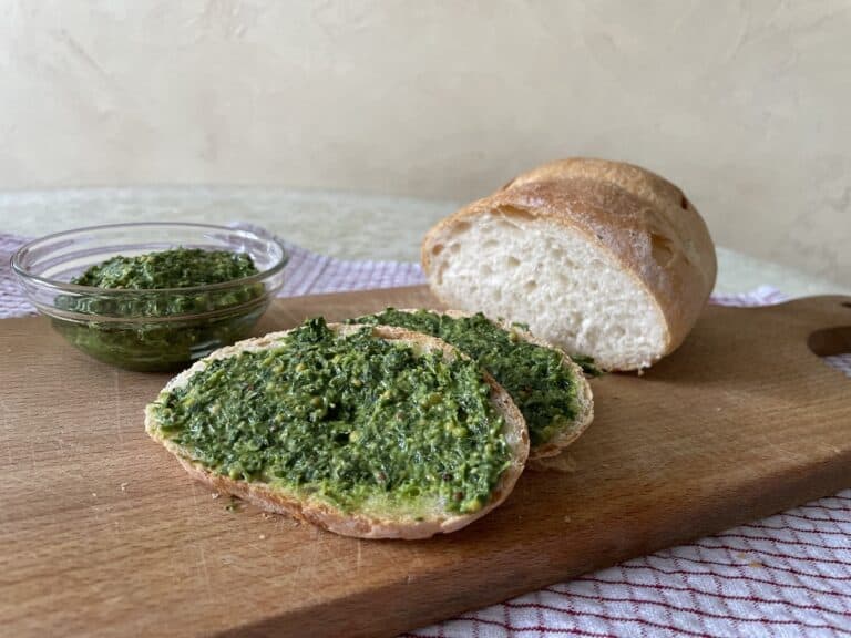 Vegan bread topped with pesto and fresh parsley on a wooden cutting board.
