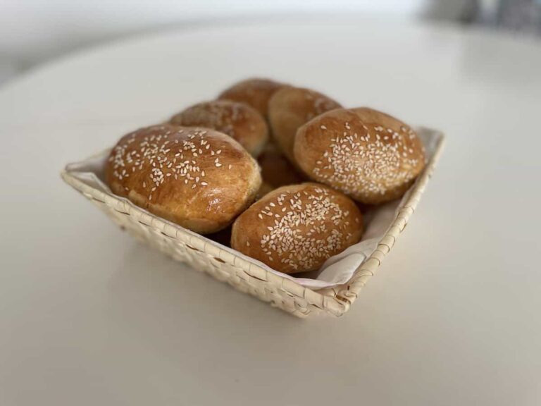 Polish hot dog buns with sesame seeds in a basket on a table.