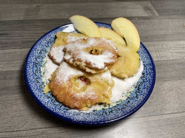 A plate with powdered sugar-dusted Polish apple pancakes without yeast and apple slices.