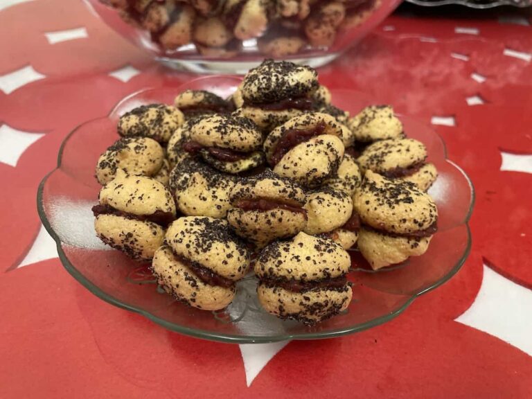 A plate of round Polish poppy seed cookies, displayed on a red patterned tablecloth.