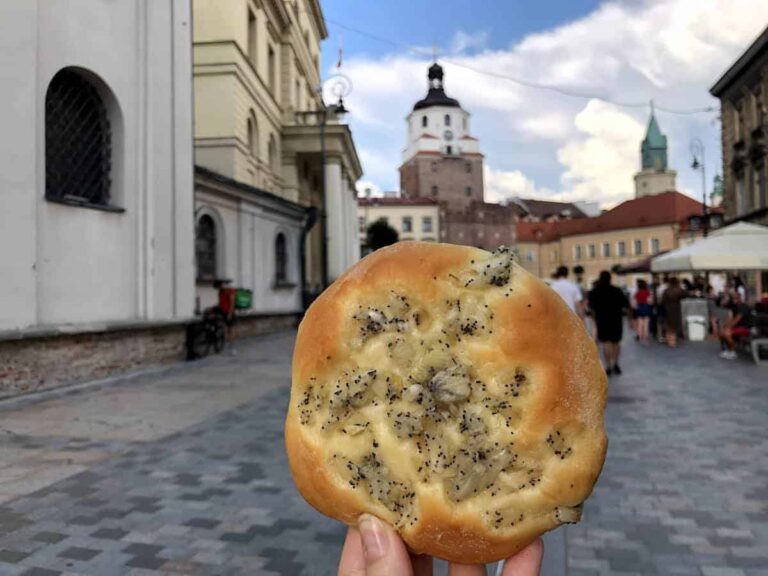 A hand holding Polish Onion Rolls with a European town square in the background.