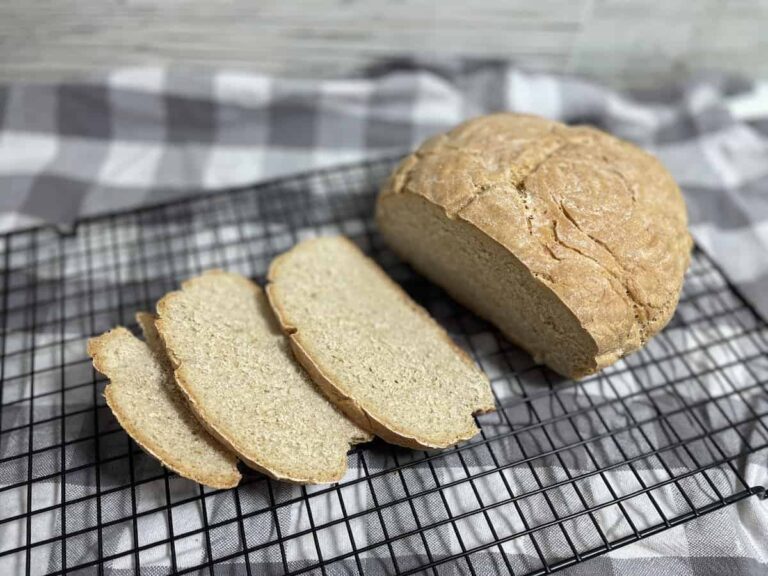 A loaf of Polish buttermilk rye bread partially sliced on a cooling rack with a checkered cloth underneath.