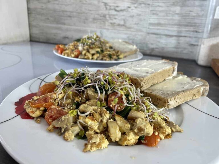 A plate of vegan tofu scramble with vegetables and sprouts served with buttered toast.