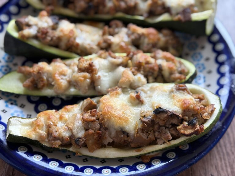 Halved zucchinis stuffed with a savory mixture of meat and vegetables, topped with melted cheese, showcase this classic Polish Stuffed Zucchini Recipe on an elegant patterned plate.