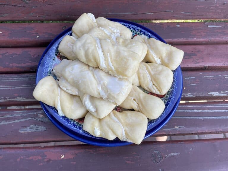 A blue plate on a weathered wooden bench holds a stack of Polish Sweet Cheese Twists, showcasing the delightful Zawijane Drożdż&oacute;wki Z Serem pastry from a traditional Polish dessert recipe.