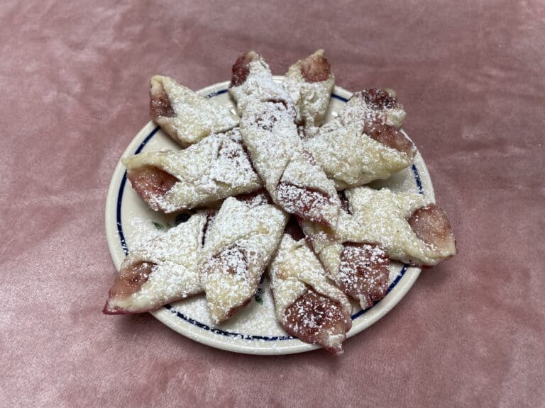 A plate of star-shaped Polish Lard Cookies, also known as Smalc&oacute;wki, dusted with powdered sugar, arranged on a pink surface.