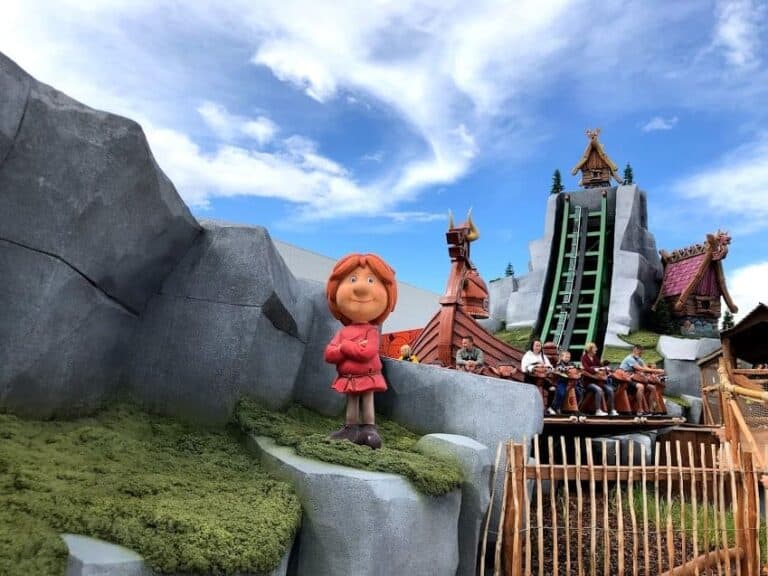 Outdoor amusement park ride with a Viking-themed statue in front, steep water slide in background, and riders descending in a log flume.