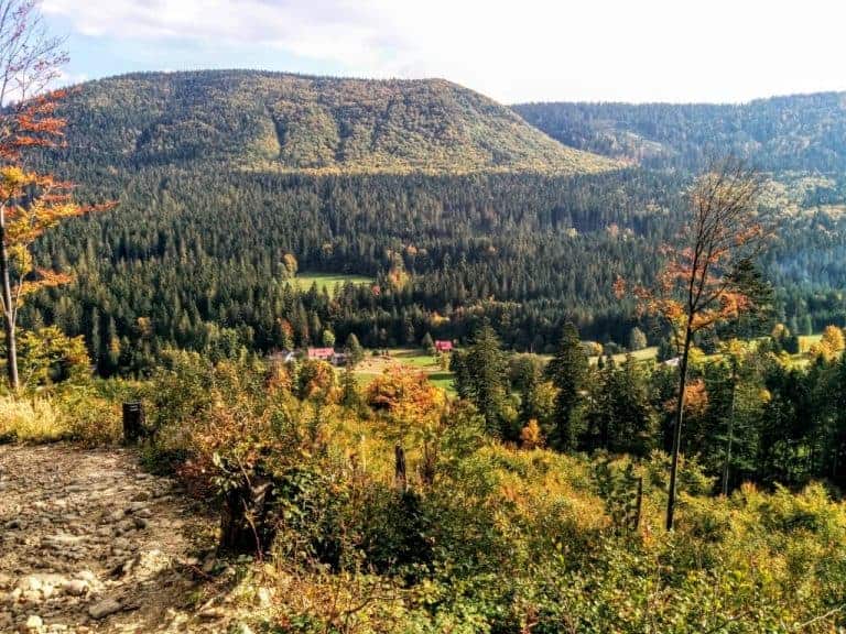 A forested valley with scattered houses, surrounded by hills and trees under a partly cloudy sky—one of the best places to see in Poland for those seeking holidays off the beaten path.