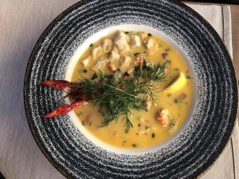 A bowl of creamy yellow seafood soup, garnished with fresh dill, croutons, lemon wedge, and crayfish claws on a speckled plate&mdash;a must-try for anyone searching where to eat authentic flavors in restaurants Wrocław offers.