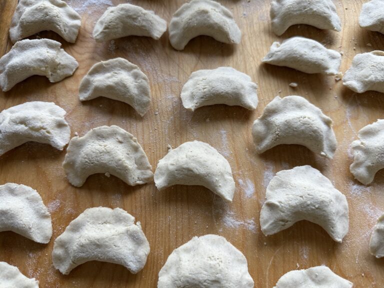 Authentic pierogi are arranged in neat rows on a wooden surface, each uncooked dumpling lightly dusted with flour.