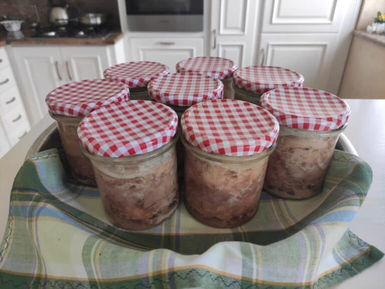 Five jars of Polish food on a table with a checkered tablecloth.