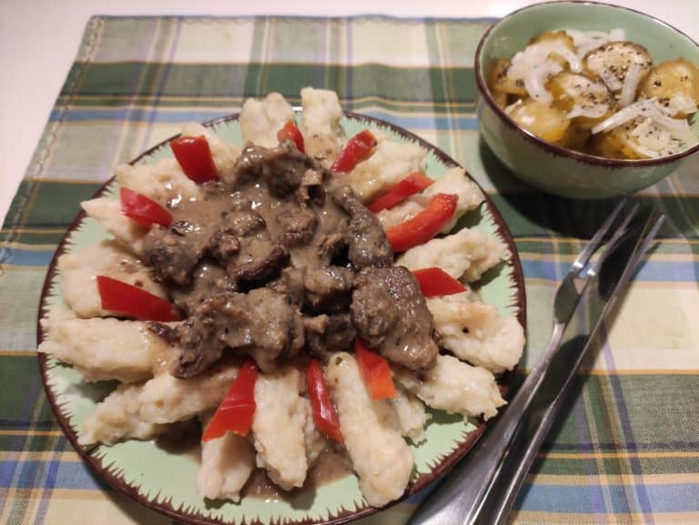A plate of kluski with mashed potatoes and meat on it.